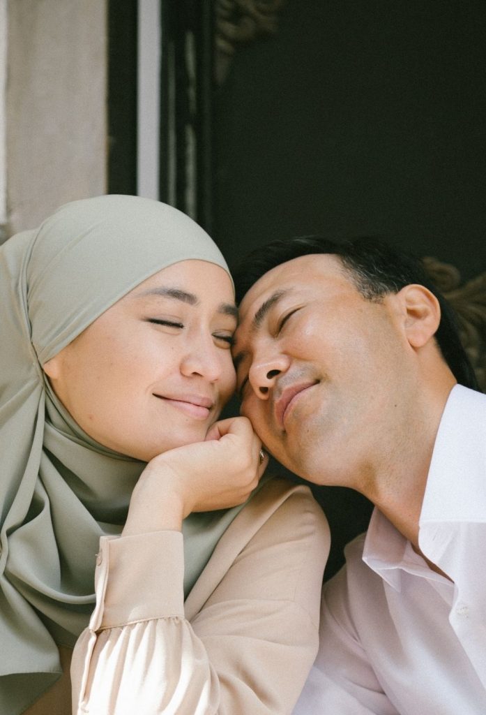 Close up of an asian couple leaning against each other with their faces touching and smiling.