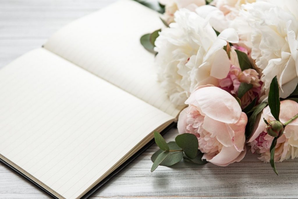 An open blank notebook with peonies arranged in front of it.