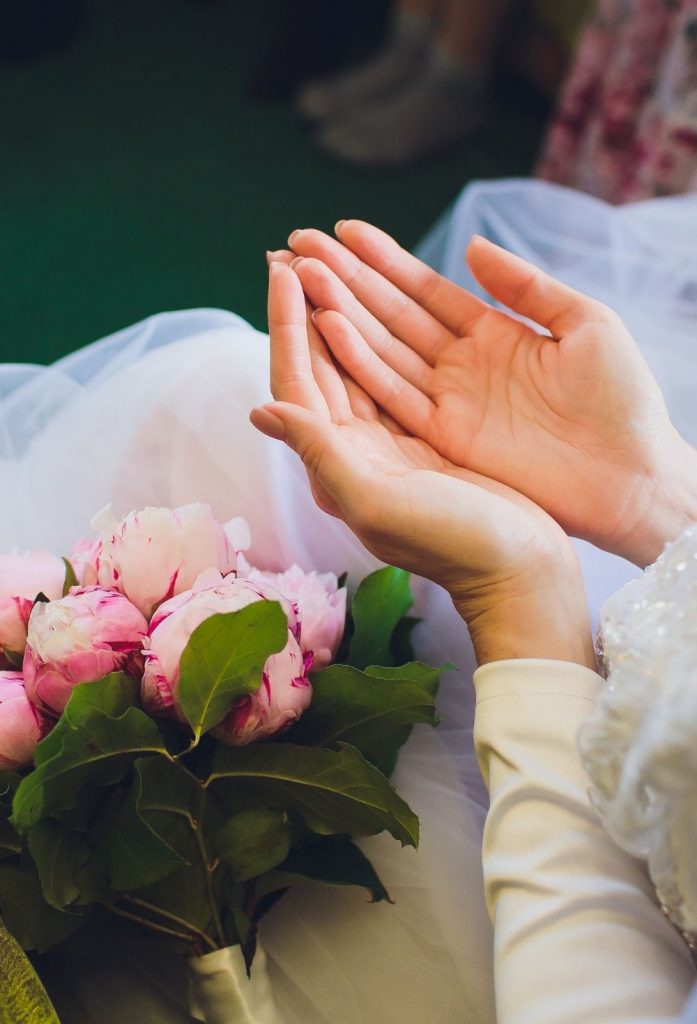 A bride's hands praying with her bouquet beside her.