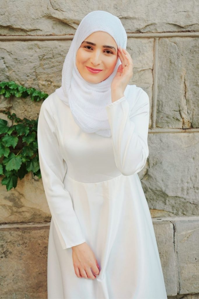 A bride in hijab wearing white smiling at the camera