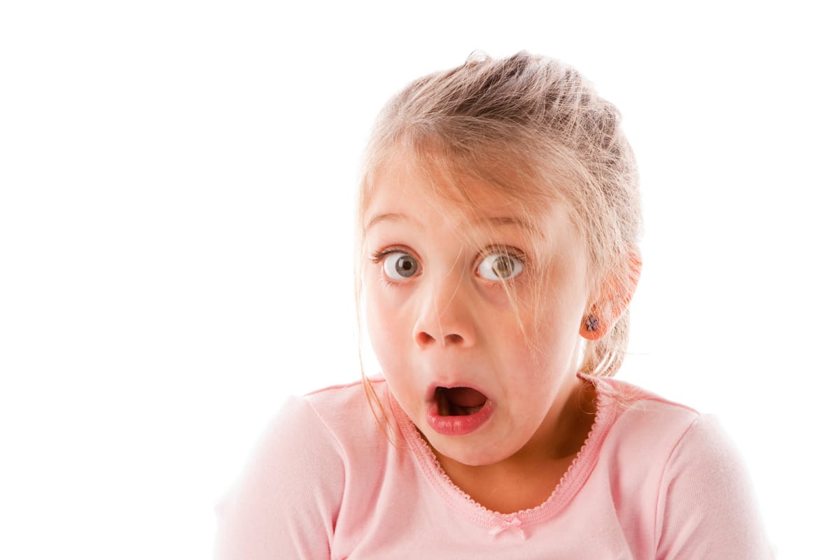 A child making an Oops face. She is wearing a pink shirt and has her mouth open